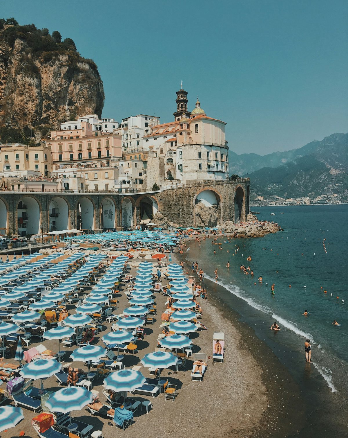 Strand van Atrani aan de Amalfikust met blauw-witte parasols en het dorp op de achtergrond